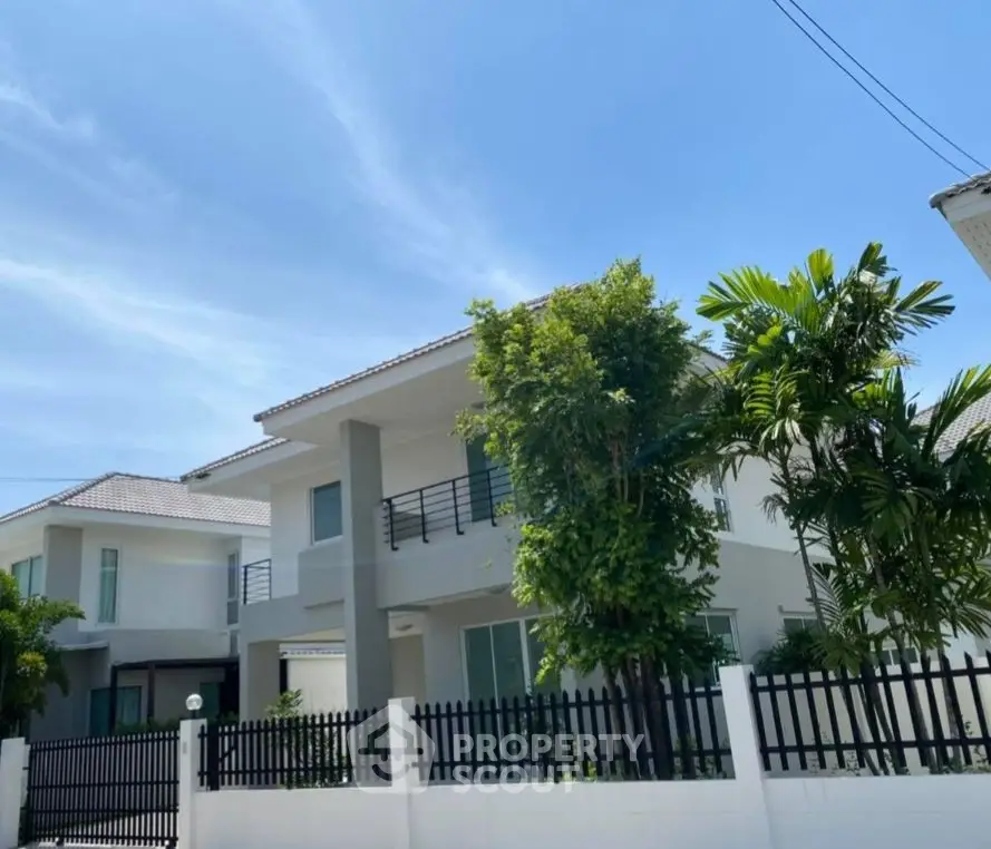 Modern two-story house with lush greenery and white fence under clear blue sky.