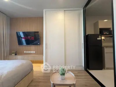 Modern bedroom with built-in wardrobe and open kitchen layout, featuring a wall-mounted TV and sleek design.