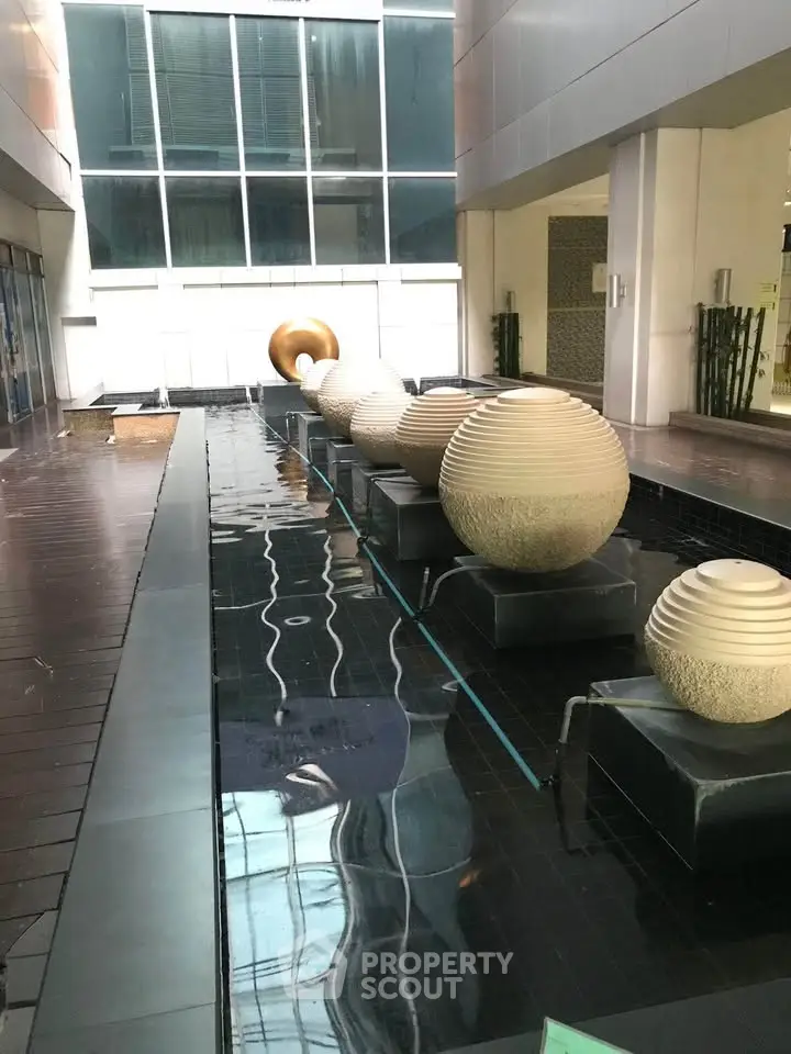 Modern building entrance with artistic water feature and sleek architectural design.