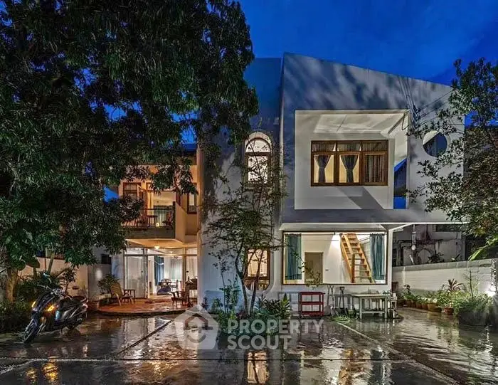 Modern two-story house with large windows and lush garden at night