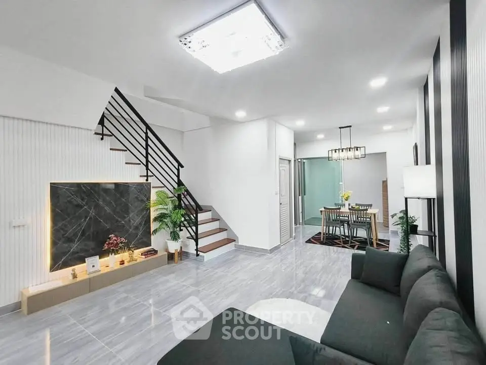 Modern living room with sleek staircase and dining area, featuring contemporary decor and ample lighting.