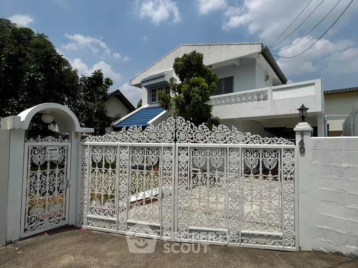 Charming two-story house with ornate white gate and lush greenery