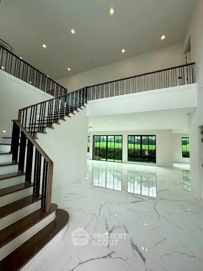 Luxurious modern interior with high ceilings and elegant staircase, featuring marble flooring and large windows.