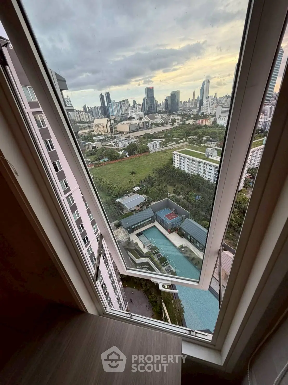 Stunning high-rise view of city skyline and pool from a modern apartment window.