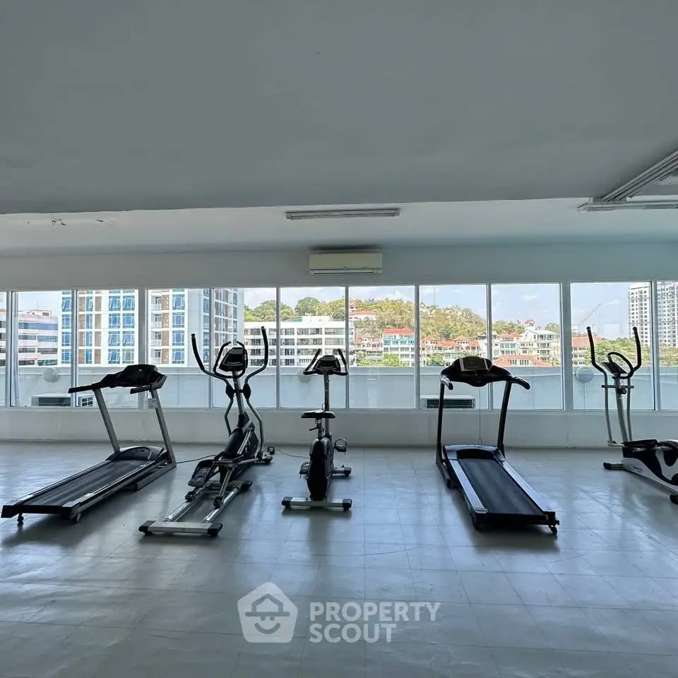 Spacious gym with modern equipment and panoramic city views in luxury apartment building.