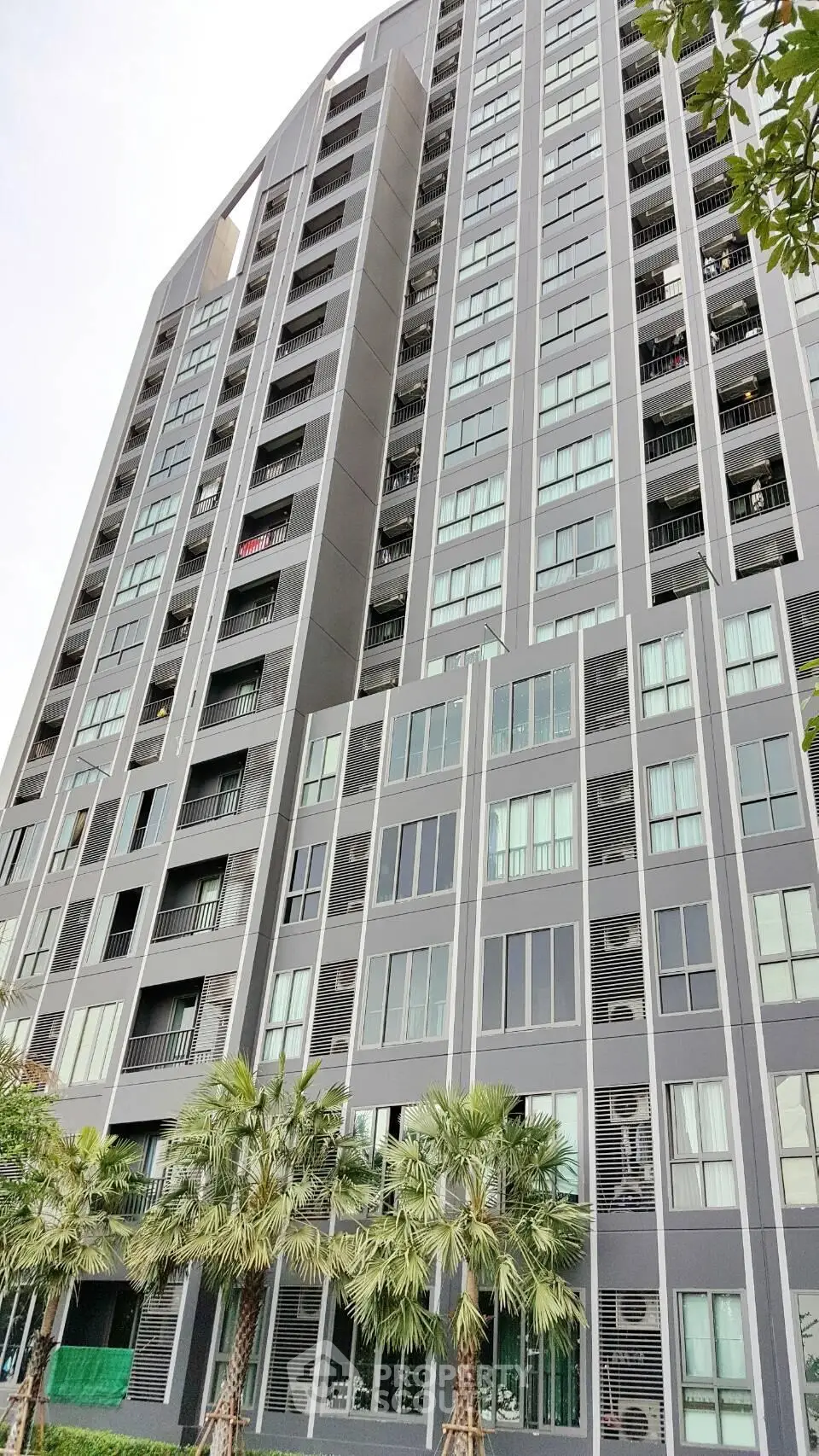 Modern high-rise building with sleek design and lush greenery at the base, offering urban living with style.