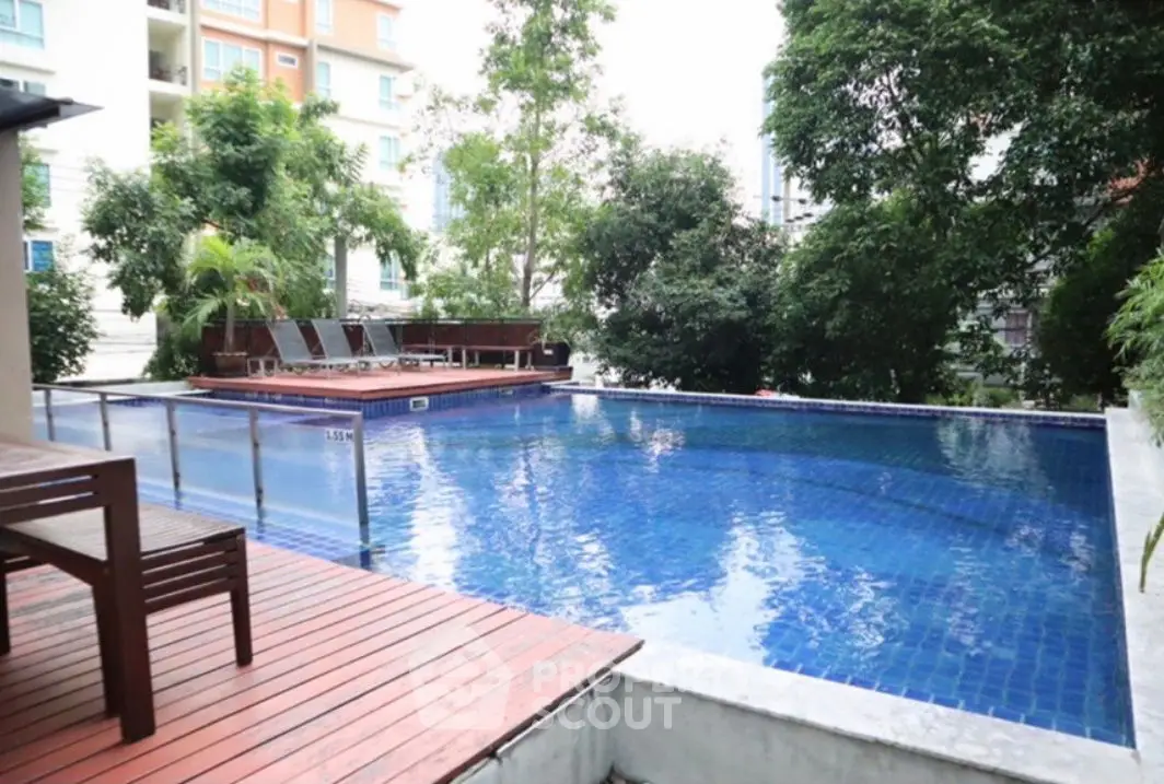 Luxurious outdoor pool area with wooden deck and lush greenery, perfect for relaxation and leisure.