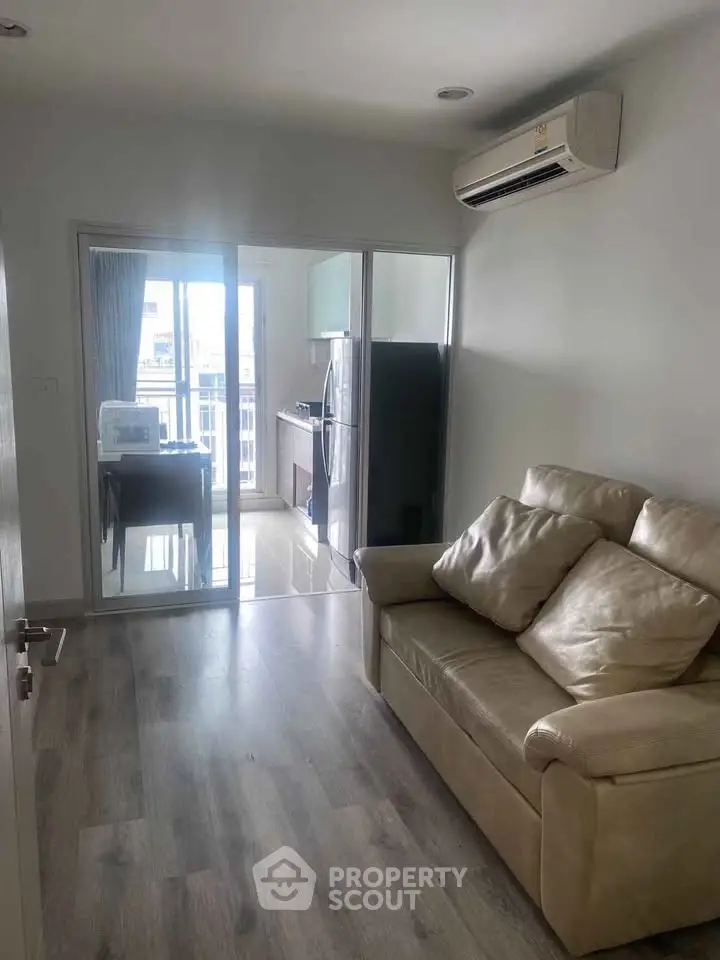 Modern living room with leather sofa and kitchen view, featuring sleek flooring and air conditioning.