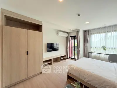 Modern bedroom with large window and balcony access, featuring sleek furniture and natural light.