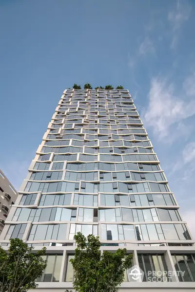 Modern high-rise building with unique architectural design and glass facade against blue sky.