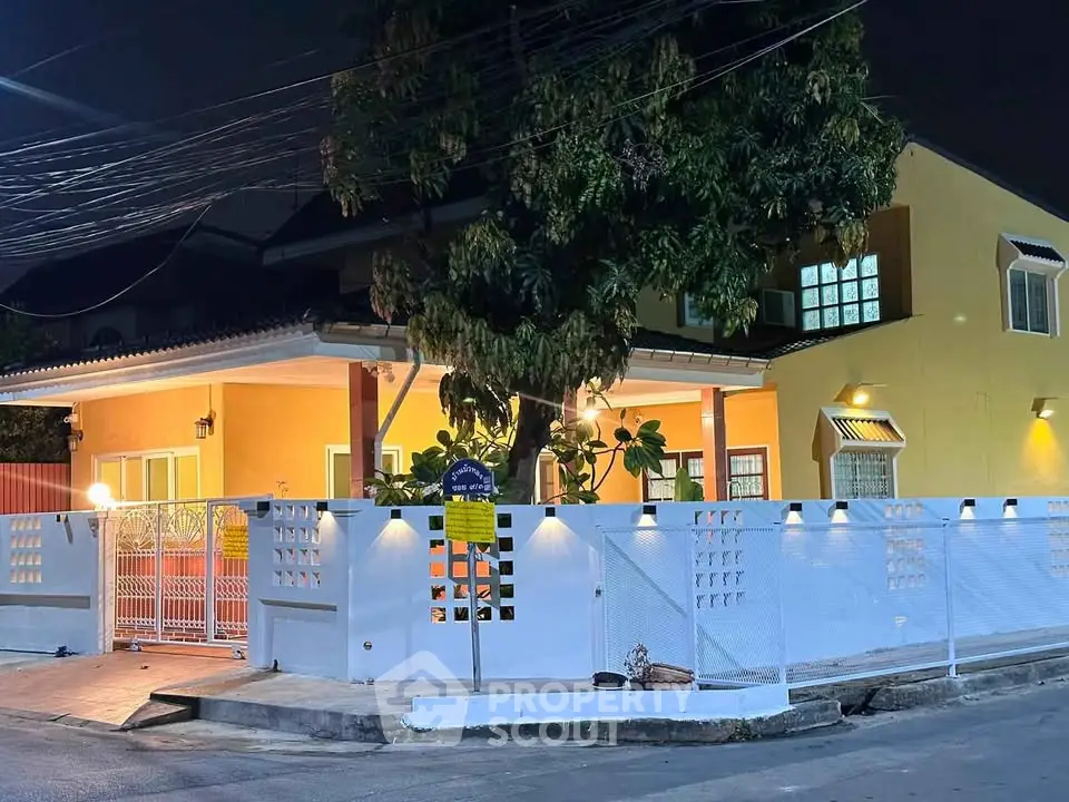 Charming night view of a cozy yellow house with a well-lit porch and white fence, perfect for family living.