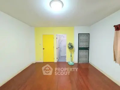Spacious room with wooden flooring and bright yellow accent wall, featuring a ceiling light and a standing fan.