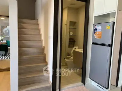 Modern interior with staircase, bathroom, and kitchen area featuring a sleek refrigerator.