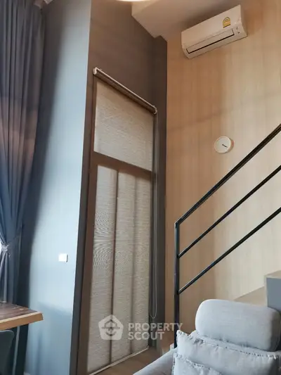 Modern living room with high ceiling and staircase, featuring air conditioning and stylish decor.