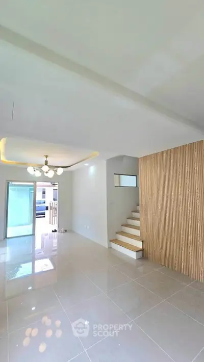 Spacious modern living room with elegant lighting and staircase, featuring glossy tiled floors and large windows.
