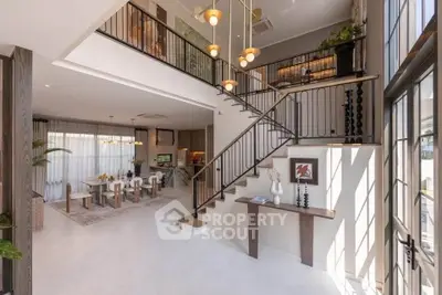 Luxurious open-plan living room with elegant staircase and modern dining area, featuring high ceilings and stylish decor.