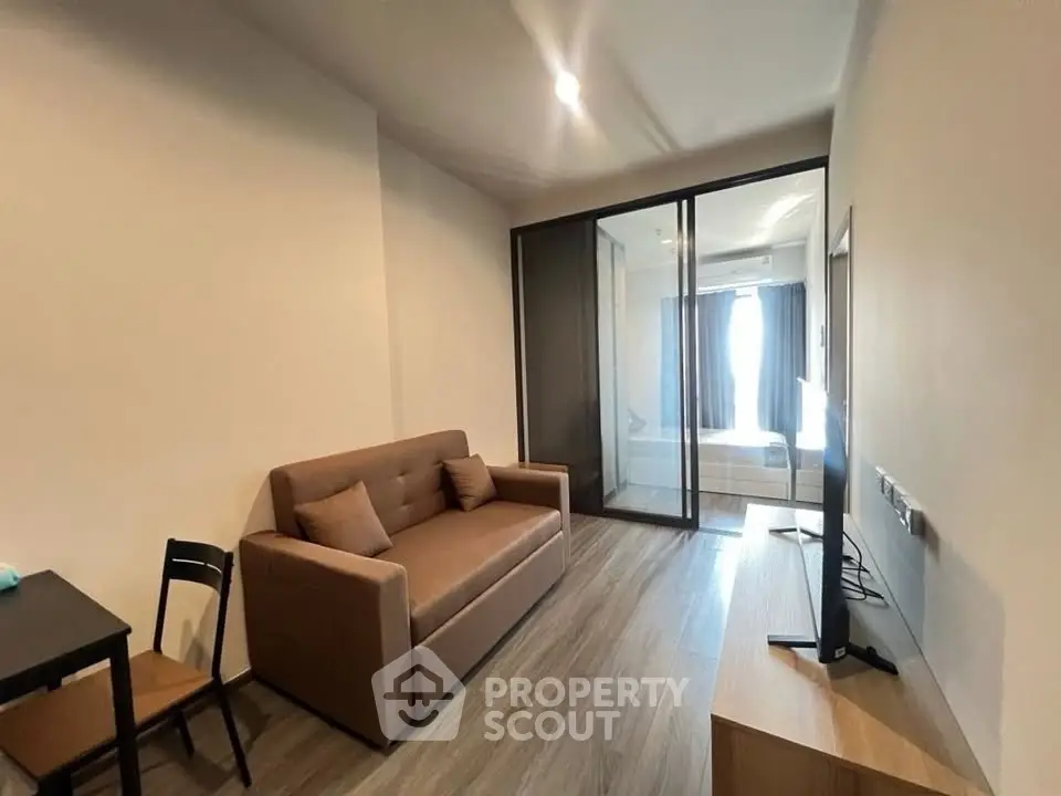 Modern living room with sleek design and glass partition leading to bedroom, featuring cozy sofa and flat-screen TV.