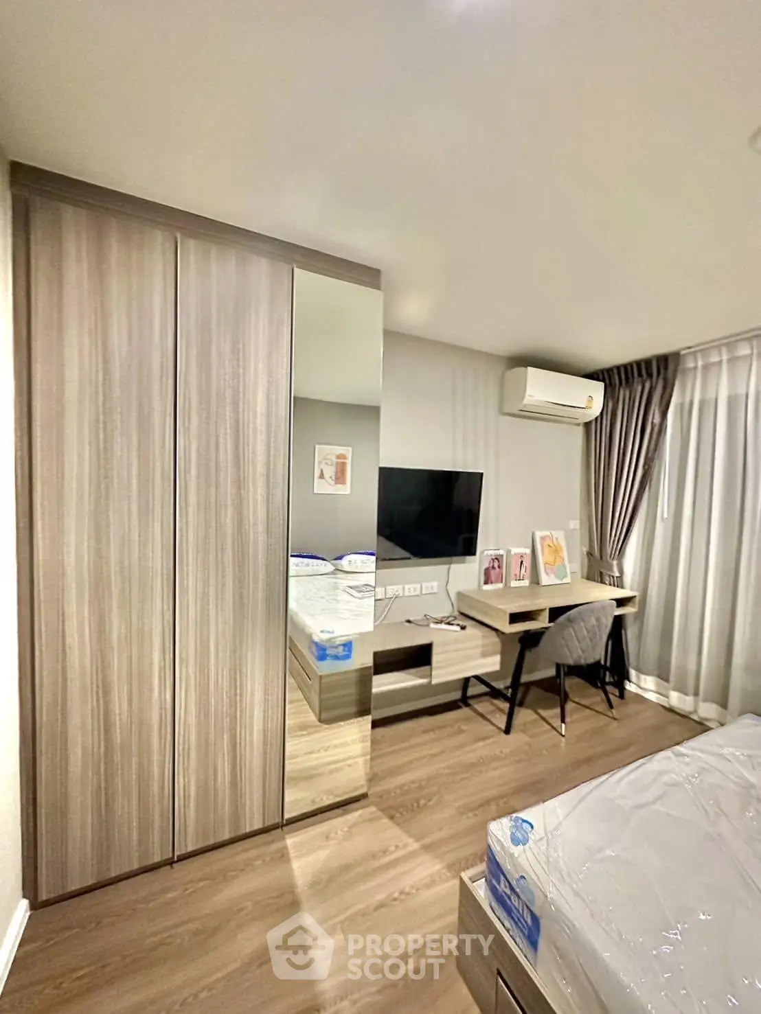 Modern bedroom with sleek wardrobe, TV, and study desk in a cozy apartment.