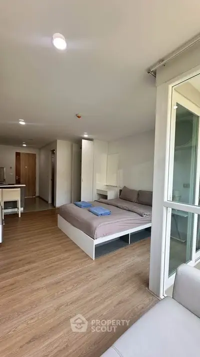Modern studio apartment with cozy bed and open layout, featuring wooden flooring and ample natural light.
