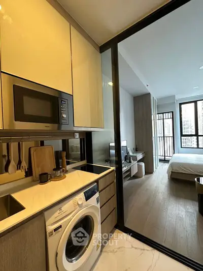 Modern apartment kitchen with washing machine and microwave, open layout to living area and bedroom.