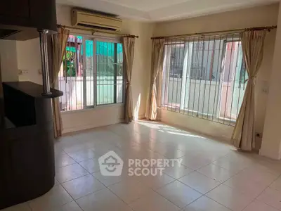 Spacious living room with large windows and natural light, featuring tiled floors and air conditioning.