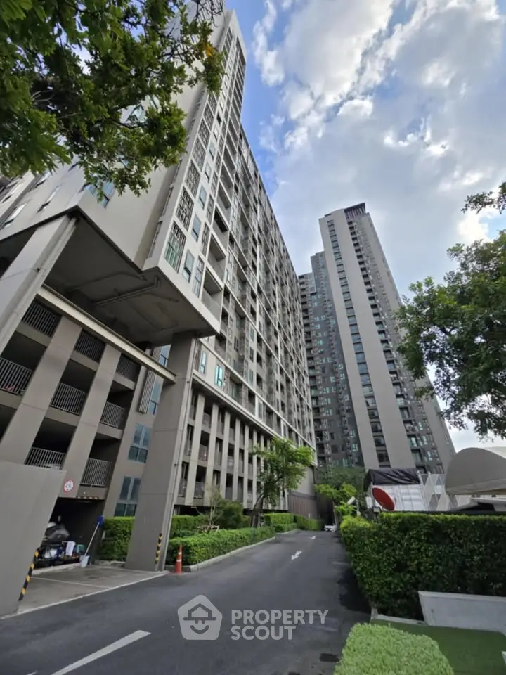 Modern high-rise residential building with lush greenery and clear sky view.