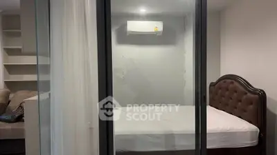 Modern bedroom with glass partition and air conditioning unit, featuring a stylish bed and cozy sofa.