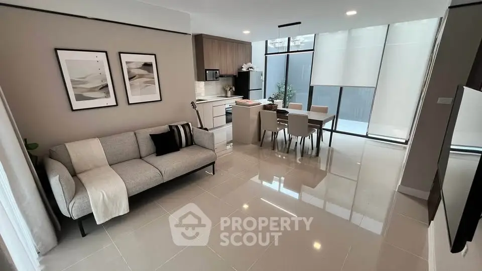 Modern open-plan living room with sleek kitchen and dining area, featuring stylish decor and natural light.