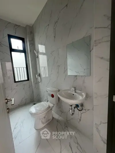 Modern bathroom with marble tiles, featuring a toilet, sink, and shower area.
