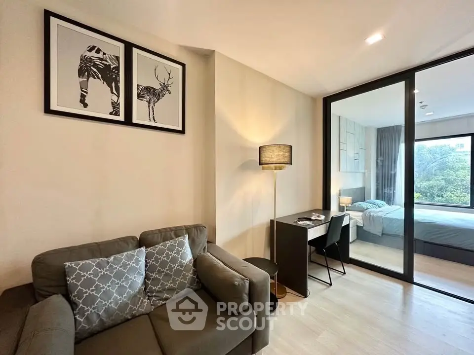 Modern living room with cozy sofa and study area, adjacent to a stylish bedroom with glass partition.