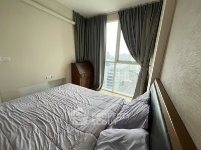Cozy bedroom with large window offering city views, featuring a comfortable bed and elegant curtains.
