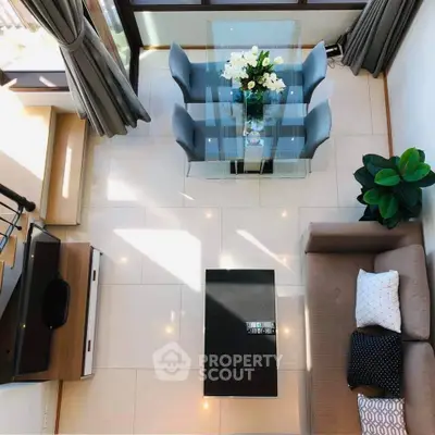 Modern living room with elegant glass dining table and cozy sofa, featuring stylish decor and natural light.