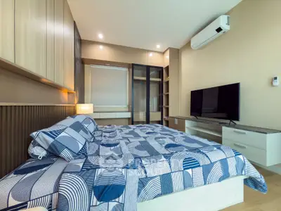 Modern bedroom with stylish decor and large TV, featuring a cozy bed and ample storage.