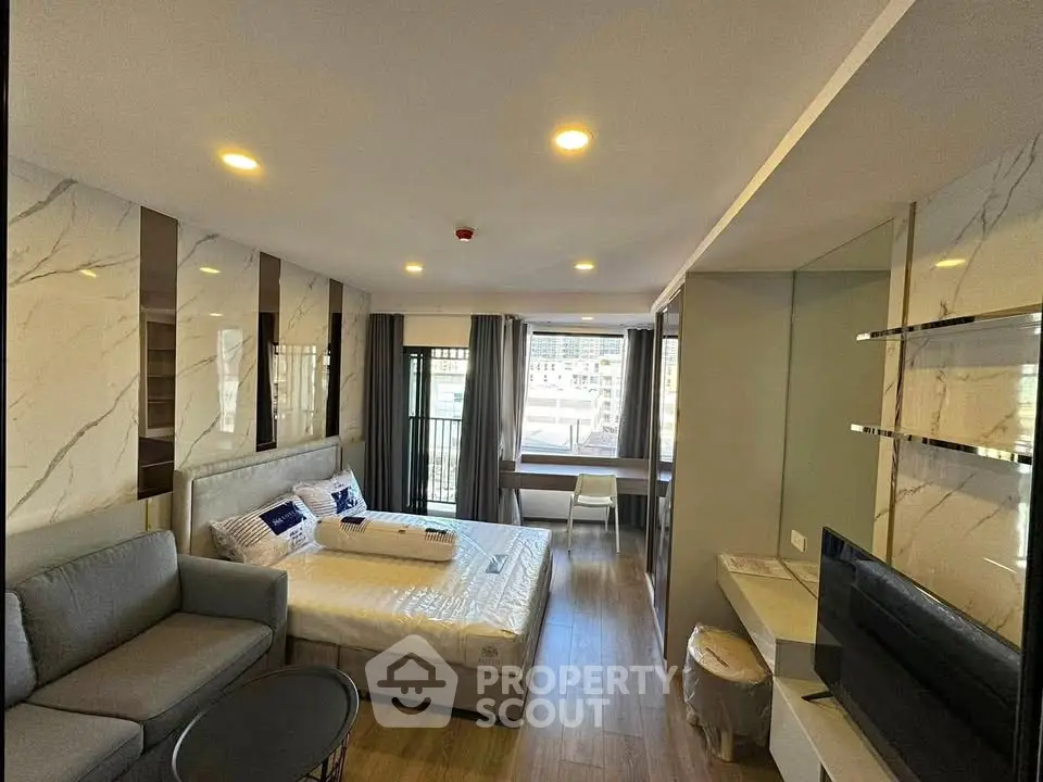 Modern studio apartment with stylish decor and natural light, featuring a cozy bed and a comfortable seating area.