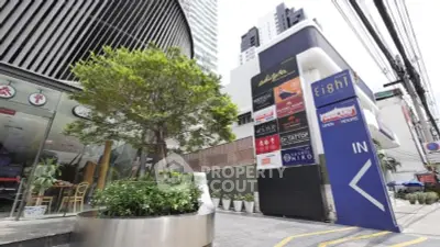 Modern commercial building entrance with signage and greenery in urban setting.