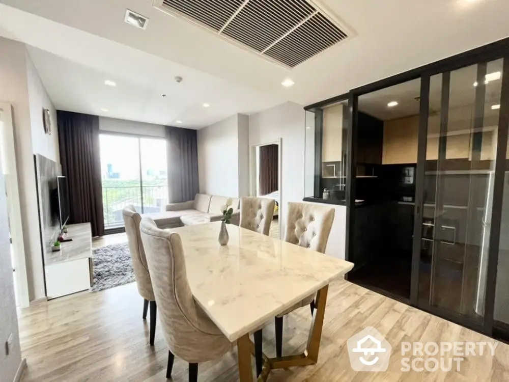 Elegant dining area seamlessly connects to a modern kitchen with sleek black cabinets, complemented by natural light from large windows.