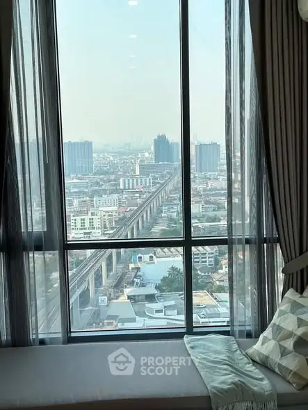 Stunning cityscape view from high-rise apartment window with cozy seating area.