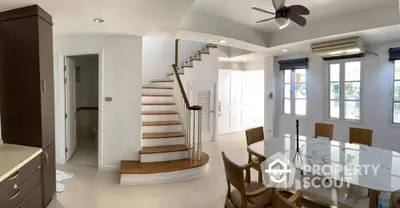 Elegant dining area with marble table and wooden chairs, featuring a stylish staircase and bright natural light.