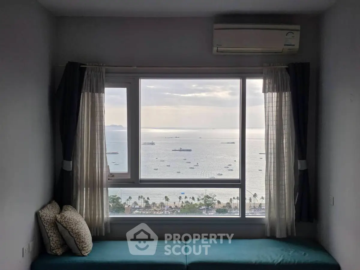 Stunning ocean view from a modern apartment window with cozy seating area.