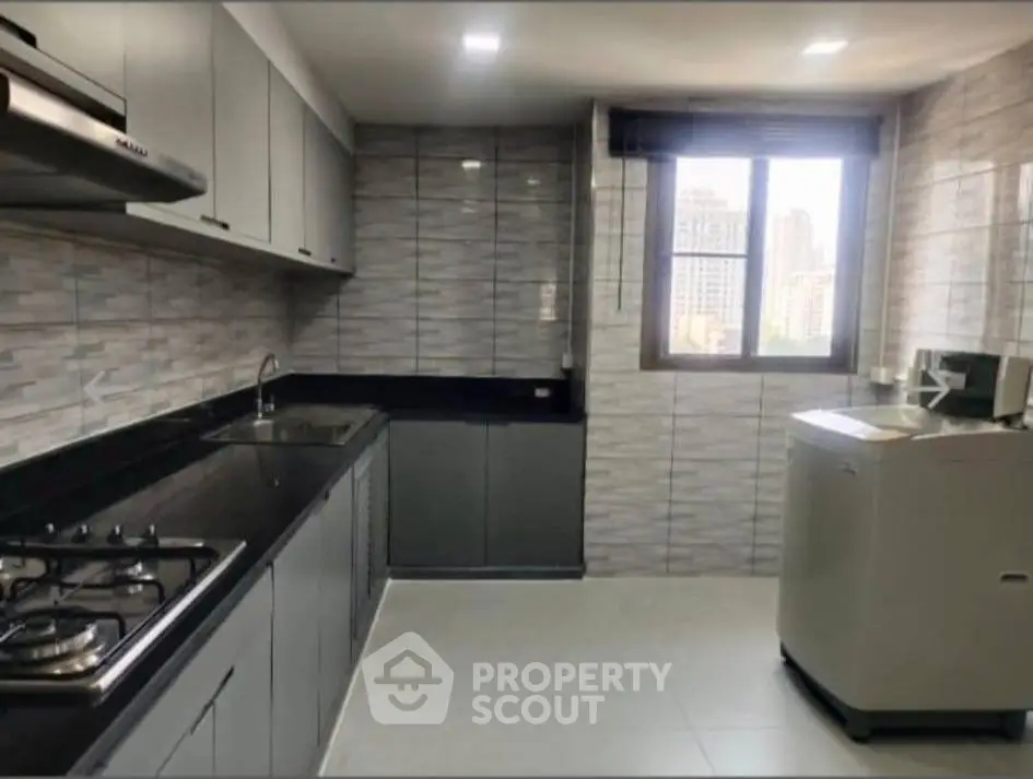 Modern kitchen with sleek cabinetry and gas stove, featuring a washing machine and city view window.