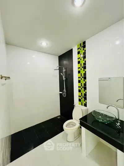 Modern bathroom with sleek black and white tiles, glass sink, and contemporary shower design.