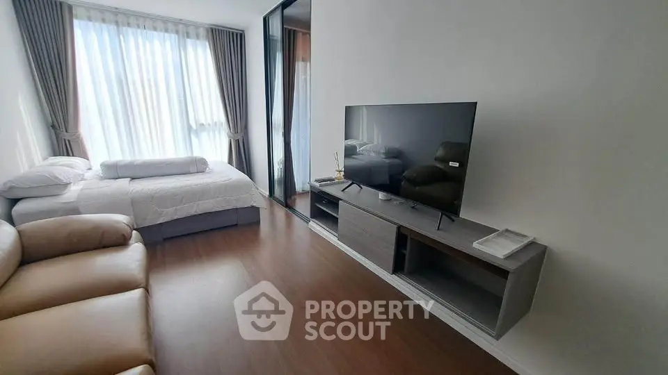 Modern bedroom with large window, cozy bed, and sleek TV setup in stylish apartment.