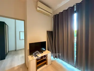 Modern living room with air conditioning and TV, featuring sleek curtains and light wood flooring.