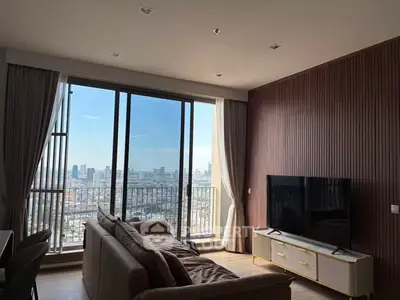 Modern living room with large windows offering stunning city views, featuring cozy seating and a sleek TV setup.