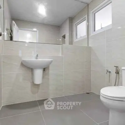 Modern bathroom with sleek tiles and contemporary fixtures, featuring a wall-mounted sink and toilet.