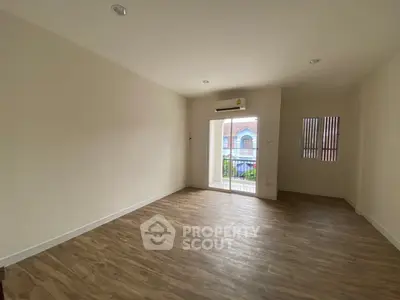 Spacious empty room with wooden flooring and large window offering natural light.