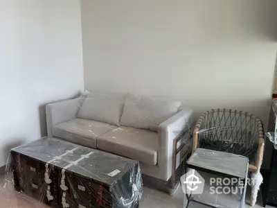 Modern living room with new furniture wrapped in plastic, featuring a stylish sofa and chair.