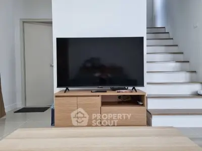 Modern living room with sleek TV stand and staircase, showcasing minimalist design and elegance.