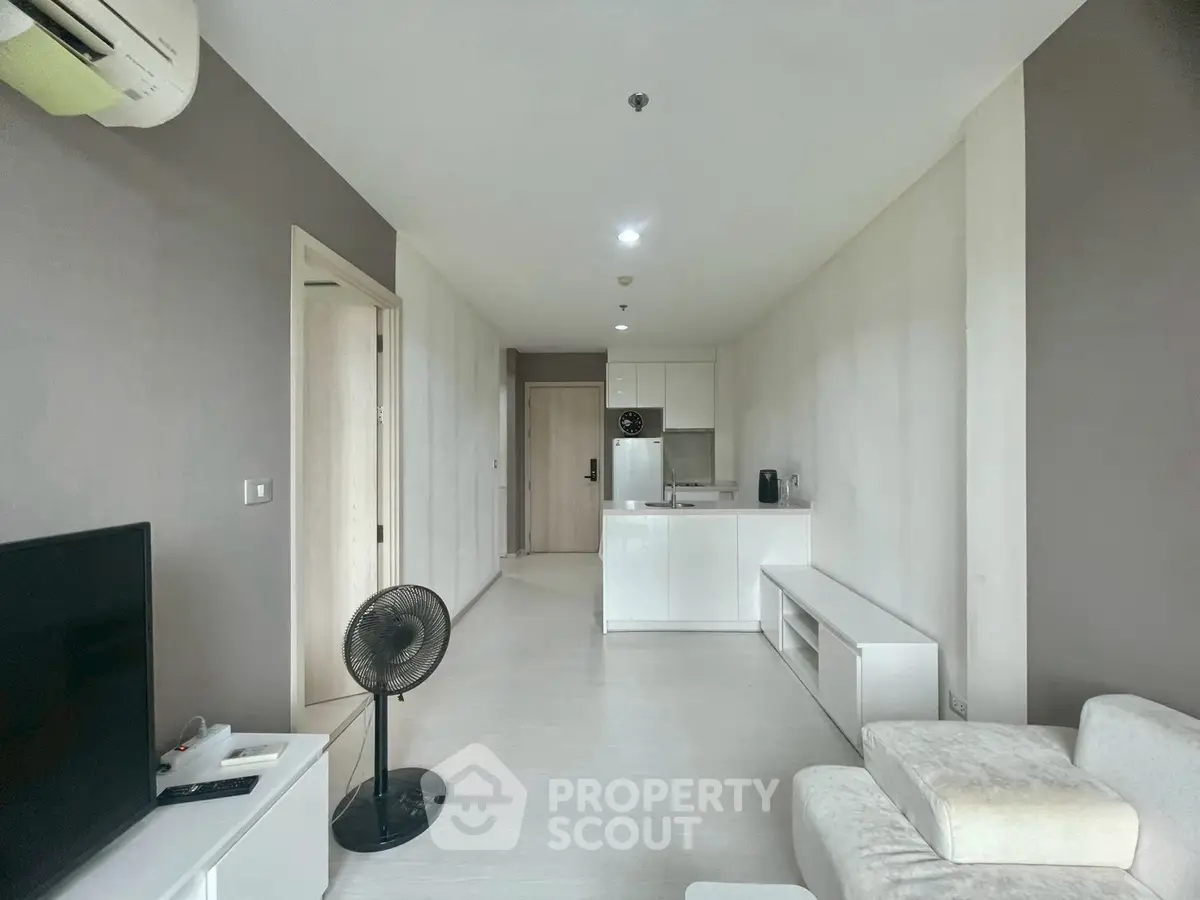 Modern living room with open kitchen layout, featuring sleek white cabinetry and minimalist decor.