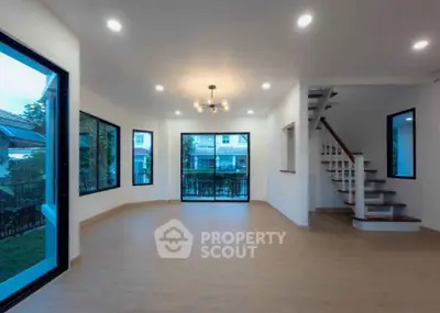 Spacious modern living room with large windows and staircase, perfect for family gatherings.